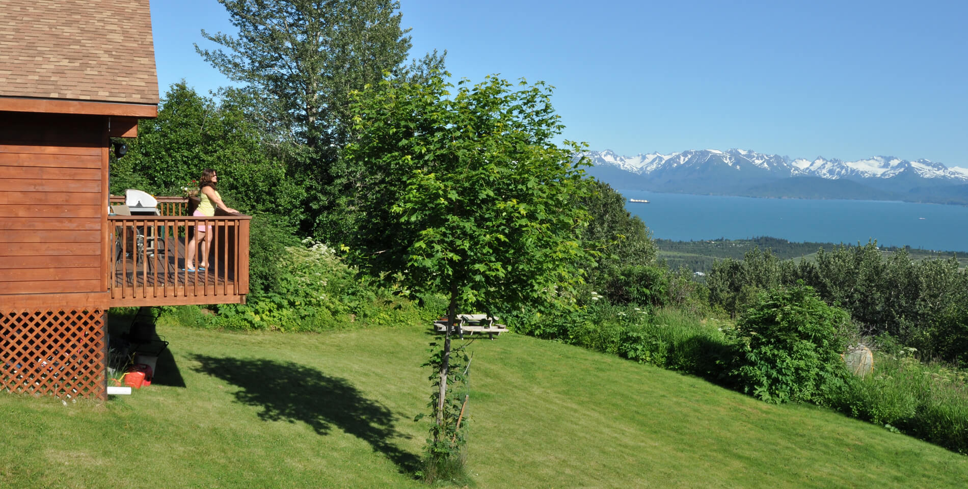 Woman standing on the deck of the cabin enjoying a sunny afternoon, viewing the bay and mountains.