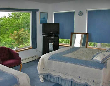 Shows room with large windows on two sides, and two queen-sized beds with blue and white bedspreads.