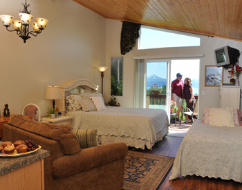 Shows a view from the doorway, corner of kitchen table with muffins, two beds, and a sliding-glass door leading to the deck.